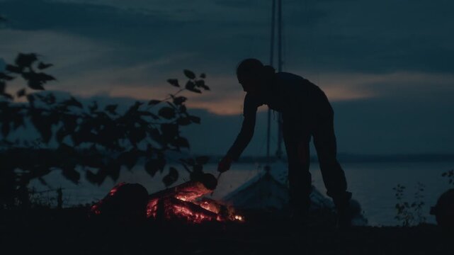 Sailing and camping in the wild. Woman sailor walks on the wild area with sailing boat on the background and bonfire on the foreground