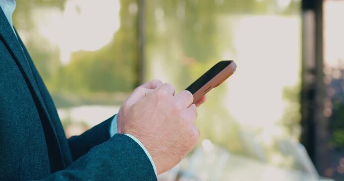 Side view of an unidentified businessman hands holding a smartphone while typing messages and scrolling through pages on the screen.