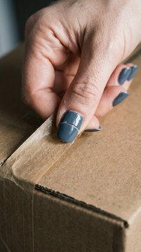 Close up of woman opening a cardboard parcel box with taped flap