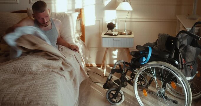 Young man with a disability gets out of bed in the morning and transfers independently into his wheelchair, beginning his daily routine at home.