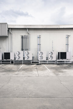 Industrial air compressor system installed beside a modern warehouse exterior with garage doors, compressed air equipment for factory operations, manufacturing, maintenance, construction and business.