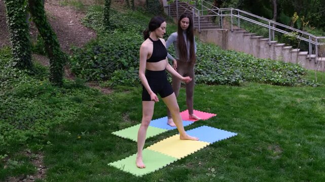Women in comfortable athletic clothing perform warm-up exercises on soft fitness mats in park. Females prepare bodies for demanding outdoor workout