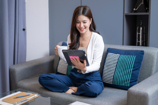 Young woman sitting on couch using tablet at home, relaxed lifestyle, smiling