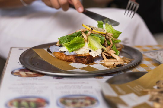 Close up of breakfast using a knife and fork to eat open faced sandwich.