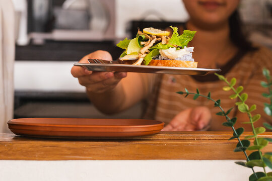 Close up of a woman serving fresh open faced sandwich topped with green salad.