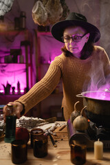 realistic witch brewing a potion in a cauldron. Everyday life intertwined with traditional witchcraft, magic and a mystical atmosphere. © Andrii Lysenko