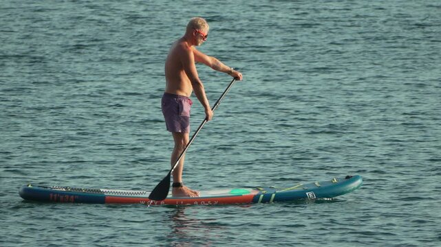 Man paddleboard ocean, shirtless man standing on a paddleboard paddling across tranquil ocean water during summer vacation
