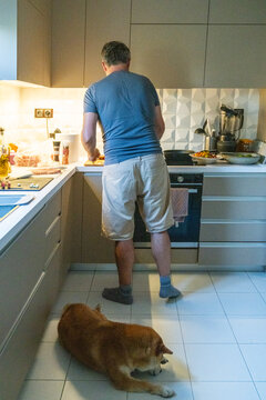 Man preparing food at kitchen counter with dog lying on floor at home