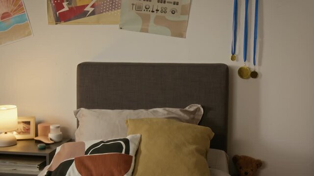 Camera tilting down from wall with sports awards to made bed in teenager bedroom. Footage ideal for student accommodation advertising and youth lifestyle marketing