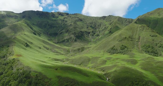 Badimalika, Bajura, Nepal, aerial sweeping shot over a wide alpine basin covered in vibrant green pastures with a meandering stream flowing down steep mountain ridges under scattered clouds