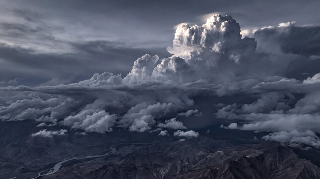 Massive thunderhead storm clouds rising above a dark mountain range viewed from high altitude