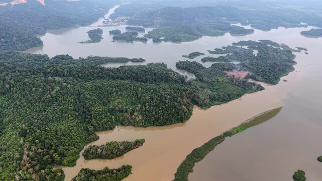 Aerial view of a wide river with brown waters. Multiple islands covered in dense green vegetation at Tasik Raban