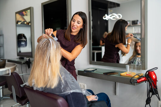 Hairdresser applying highlights to client hair in beauty salon with brush