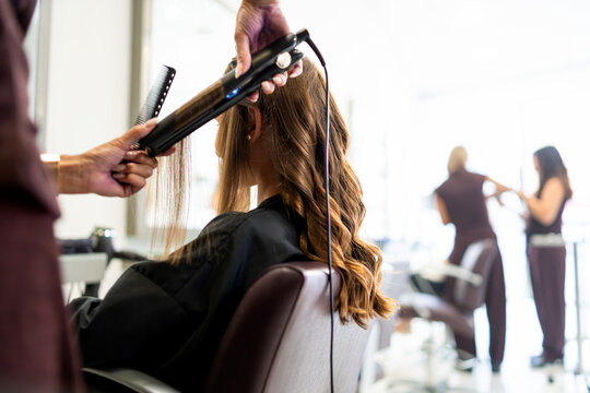 Hairdresser styling woman's hair with a curling iron in a modern beauty salon