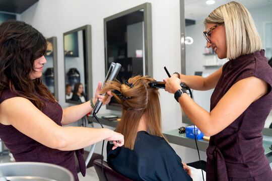 Hairdressers working together, styling client's hair in modern beauty salon