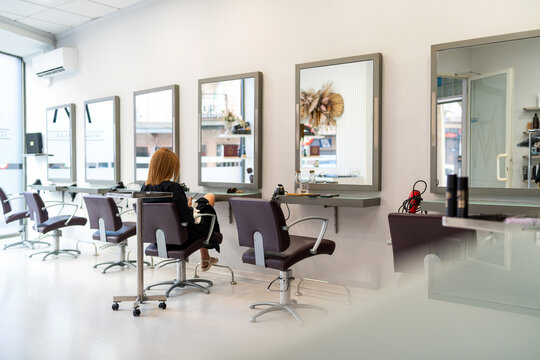 Hair salon interior featuring stylist in work chair and multiple mirrors