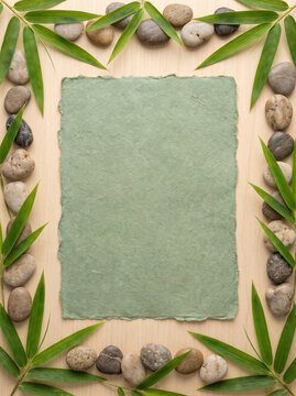Green textured paper frame with bamboo leaves and river stones on wood background