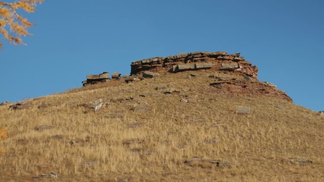 Red Devonian sandstone rock formation known as Tarpig fortress stands on a dry grass hill under a clear blue sky. Beautiful historical autumn landscape in Khakassia, Russia.
