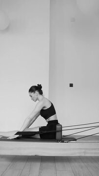 Pilates reformer training machine. woman practices pilates on reformer machine using attached straps for arm movements. Controlled resistance from springs supports strength and coordination.