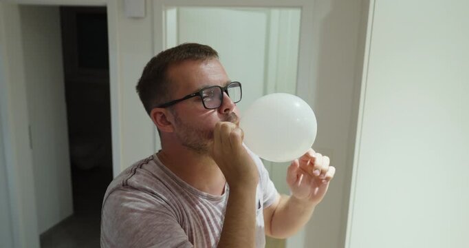 Man blows up a white balloon, becomes exhausted and out of breath, then releases the air from the balloon.