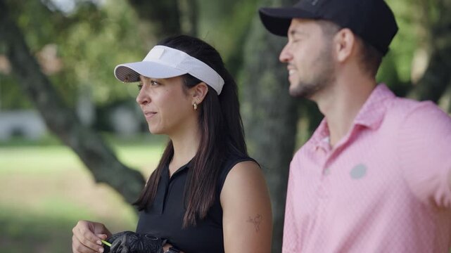 Young man and woman smiling and talking while playing golf together. This happy couple enjoys a beautiful summer day on the golf course