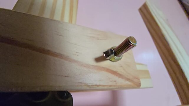 A close-up macro shot highlighting a metal bolt and nut securing a wooden frame structure or artist easel.   