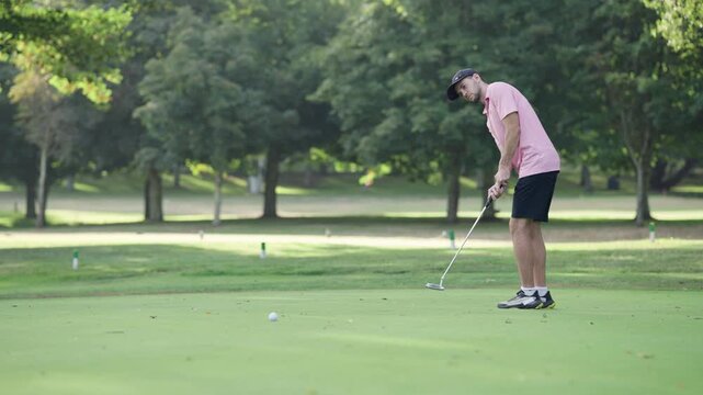 Professional golfer on the green concentrating and hitting the ball with a putter. Man playing a game of golf during a tournament