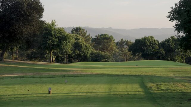 Idyllic view of a beautiful golf course with a green, fairway, and teeing ground. Sunny day with long shadows and hills in the background