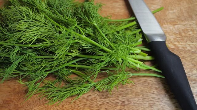 Fresh dill placed on a wooden cutting board next to a kitchen knife, showing a common herb used in cooking.