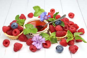 Fresh organic raspberries with tartlets, fresh green mint leaves, and purple cornflowers on white wooden background, sweet summer berry dessert © Andrii