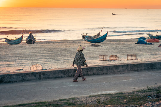 Person walking along a beach with fishing boats