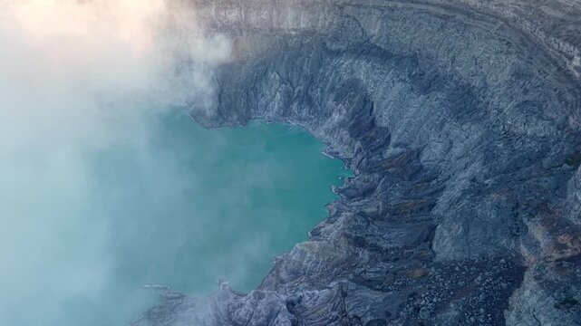 Vibrant turquoise water fills volcanic crater. Misty steam rises from the crater depths at Mount Ijen