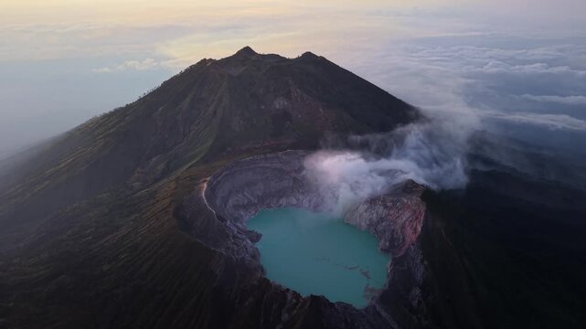 Drone panorama of Mount Ijen crater with turquoise lake, rising steam and cloud inversion at sunrise.