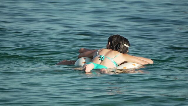 Children relaxing and playing together on inflatable pool float in ocean waves. Static medium shot.