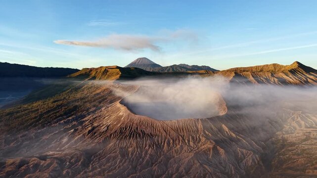 Golden sunrise illuminates Mount Bromo caldera with drifting mist and rugged volcanic ridges.