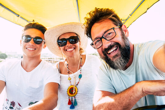 Smiling family enjoying a sunny boat ride: father with beard, mother in sun hat and necklace, teenage son in sunglasses sharing laughter and summer vacation together on the water.
