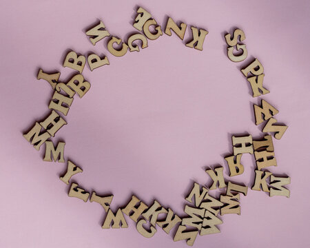 Circular frame made of jumbled wooden letters, with a blank space in the center and a light pink background.