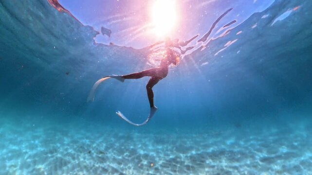 Freediving woman swimming gracefully with long fins over sandy seabed in crystal clear turquoise sea. Wide angle underwater shot.