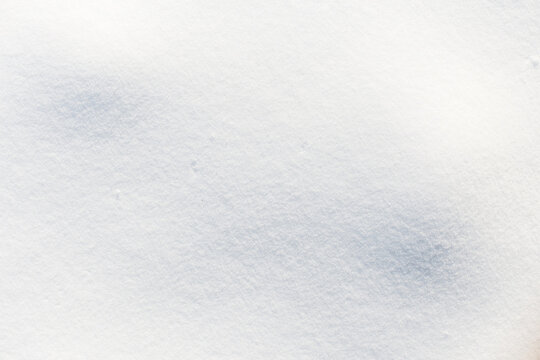 Smooth fresh white snow surface texture illuminated by soft winter light. Clean pure snowdrift background with gentle fine grain detail. Ideal seasonal wallpaper with copy space.