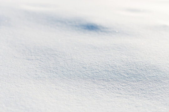 Fresh white snow surface texture illuminated by bright winter sunlight. Soft glittering snowdrift layer outdoors on a freezing cold day. Abstract seasonal background with copy space.