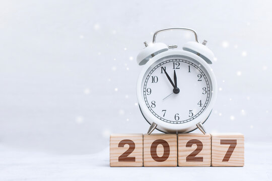 White vintage alarm clock on wooden 2027 blocks with copy space for text. New Year countdown, business planning or calendar year concept.