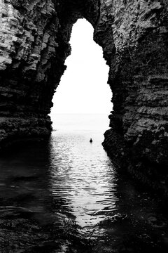 Natural sea cave in the cliffs at Flamborough Head, East Yorkshire, opening onto the North Sea. Dramatic black and white view with strong rock textures and reflections.