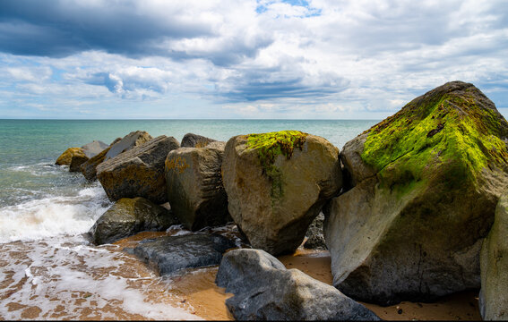 Massive sea defence boulders covered in vivid green algae at Horsey Gap, Norfolk, with waves breaking beneath a dramatic summer sky over the North Sea.