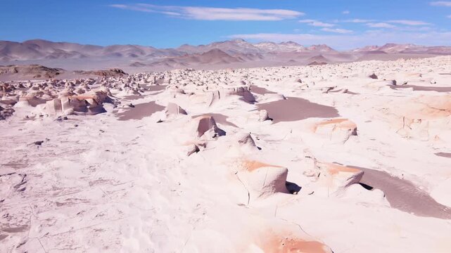 White pumice rock fields stretch toward distant Andean mountains under clear blue sky in Campo de Piedra P&oacute;mez, Catamarca, Argentina.