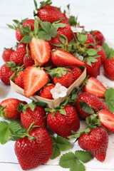 Fresh organic ripe strawberries whole and halved with small wooden basket, green leaves, and white flowers on white wooden background, summer berry © Andrii