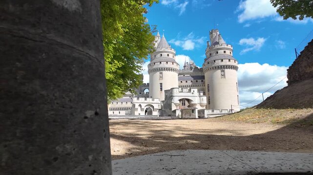 Slow motion reveal of Ch&acirc;teau de Pierrefonds emerging from behind a stone wall, showing its round towers, turrets and fortified architecture