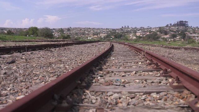 Low angle along abandoned railway tracks curving toward dense township housing on a sunny day.
