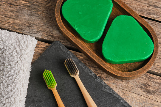 Close up eco friendly bathroom products with wooden toothbrushes, solid shampoo, and towel.
