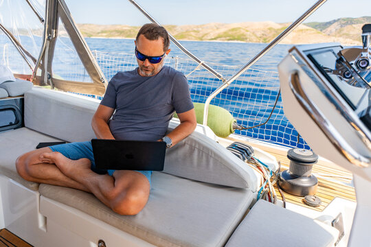 Focused man working on laptop aboard a sailing yacht. Productive remote office in a unique travel environment.
