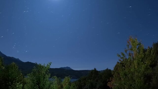 Full moon setting and star trails over mountains and Lac de Serre-Poncon  at night, French Alps, France, Europe. Night sky with stars moving over a mountain lake Lac de Serre-Poncon, Alpes-de-Haute-Pr